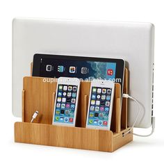 three cell phones are in a wooden holder with charging cords on the sides and one is plugged into an external charger