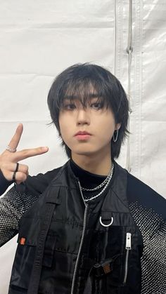 a young man with black hair and piercings making the peace sign in front of a white backdrop