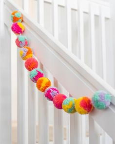 colorful pom - pom garland hanging on the railing of a white crib