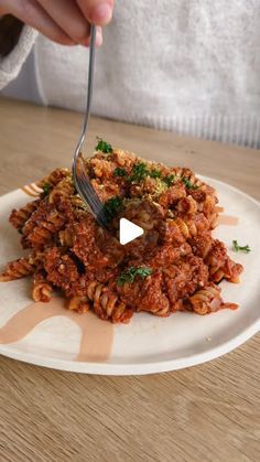 a person is holding a fork over some food on a white plate with parsley