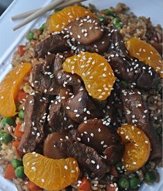 a white plate topped with meat and oranges on top of rice next to chopsticks