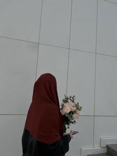 a woman in a red shawl is looking at her cell phone and holding flowers