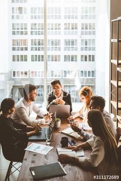 a group of people sitting around a table with laptops and papers in front of them