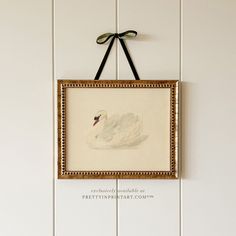 a white swan is hanging on the wall next to a frame with a black bow