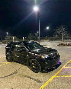 a black jeep parked in a parking lot at night with street lights on the side