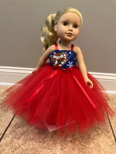 a doll with blonde hair wearing a red tutu skirt and blue top, standing on the floor