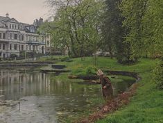 an old man standing next to a body of water in the middle of a lush green park