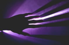 the shadow of a person's hand on a purple wall with light coming through it