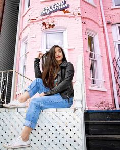 a woman sitting on the ledge of a pink building