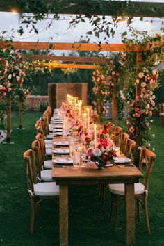 an outdoor dinner table set with candles and flowers on the tables, surrounded by greenery