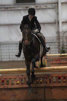 a person riding on the back of a brown horse over an obstacle in front of a building