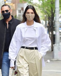 a man and woman walking down the street wearing face masks