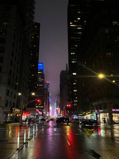 a city street at night with cars driving on the road and tall buildings in the background