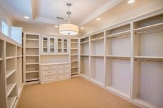 an empty walk in closet with lots of white shelves and drawers on either side of the closet