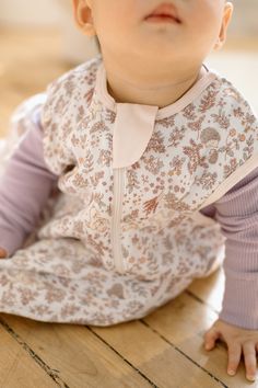 a baby is sitting on the floor wearing a pink and white outfit with floral print