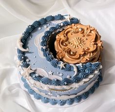 a blue and white cake with gold decorations on it's top sitting on a white sheet