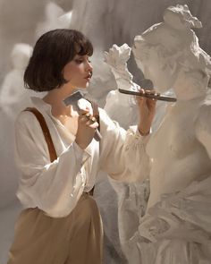 a woman holding a paintbrush in her right hand and looking at an angel statue