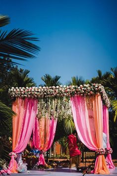 an outdoor wedding setup with pink and orange draping, white flowers and greenery