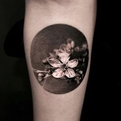 a black and white photo of a flower in a circle tattoo on the right forearm