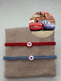 two bracelets with cars on them sitting next to each other in front of a piece of fabric