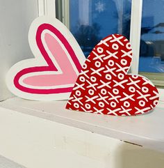 two heart shaped paper cut outs sitting on a window sill next to each other