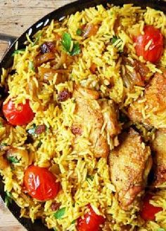 chicken and rice with tomatoes in a skillet on a wooden table top, ready to be eaten