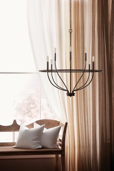 a chandelier hanging from the ceiling in front of a window with sheer curtains