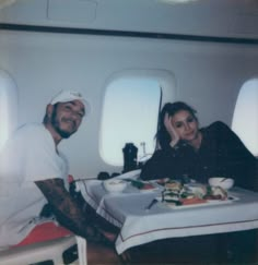 a man and woman sitting at a table with food in front of them on an airplane