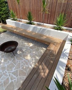 a wooden bench sitting on top of a stone floor next to a planter filled with potted plants