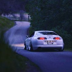 a white sports car driving down a road next to lush green trees and bushes at night