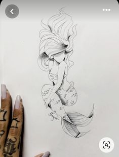 a drawing of a mermaid sitting on top of a piece of paper