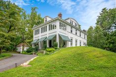 a large white house sitting on top of a lush green hillside in front of trees