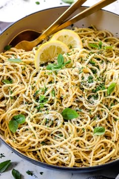 a skillet filled with pasta and topped with parmesan cheese, lemon wedges and fresh herbs