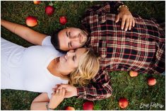 a man and woman laying on the grass with apples around them in front of them