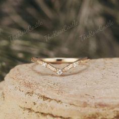 a gold wedding band with three diamonds on top of a piece of rock in front of some trees