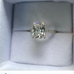 an engagement ring with a cushion cut diamond in it's box on top of a white cloth