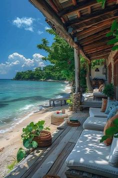 an outdoor covered porch overlooking the ocean and sandy beach with wicker furniture on it