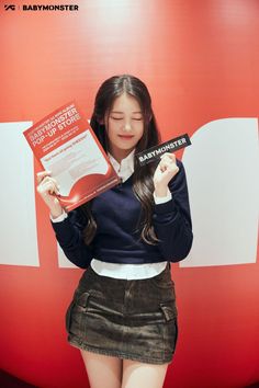 a young woman holding up a book in front of her face while standing next to a red wall