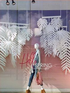 a woman's clothing store window display with white paper cut outs and palm leaves