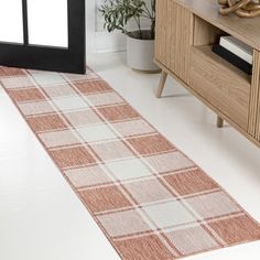 a white and red rug on the floor in a room with a wooden cabinet, plant and mirror