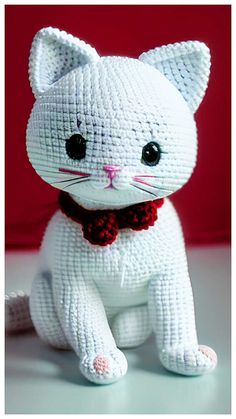 a white cat with black eyes and a red bow tie sitting on a table next to a red wall