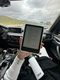 a person sitting in the driver's seat holding up an electronic device with a book on it