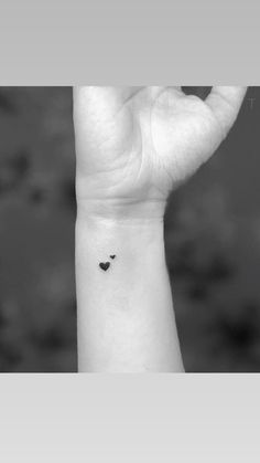 a small black heart tattoo on the left inner wrist, with an arrow in the middle