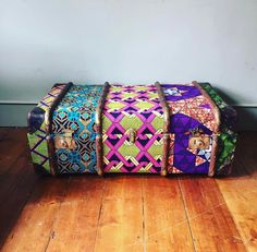 a multicolored piece of luggage sitting on top of a wooden floor next to a wall