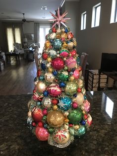 a brightly colored christmas tree with ornaments on it's base in a living room