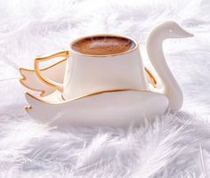 a white swan shaped coffee cup and saucer sitting on top of a feathery surface