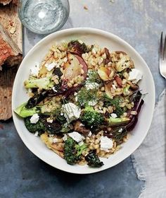 a white bowl filled with rice and vegetables next to a slice of bread on top of a table