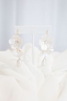 a pair of white flowers and pearls are hanging from the back of a mannequin