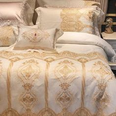 a bed with white and gold comforter in a bedroom next to a night stand