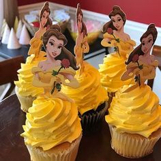 some cupcakes with yellow frosting and princess faces on them sitting on a table